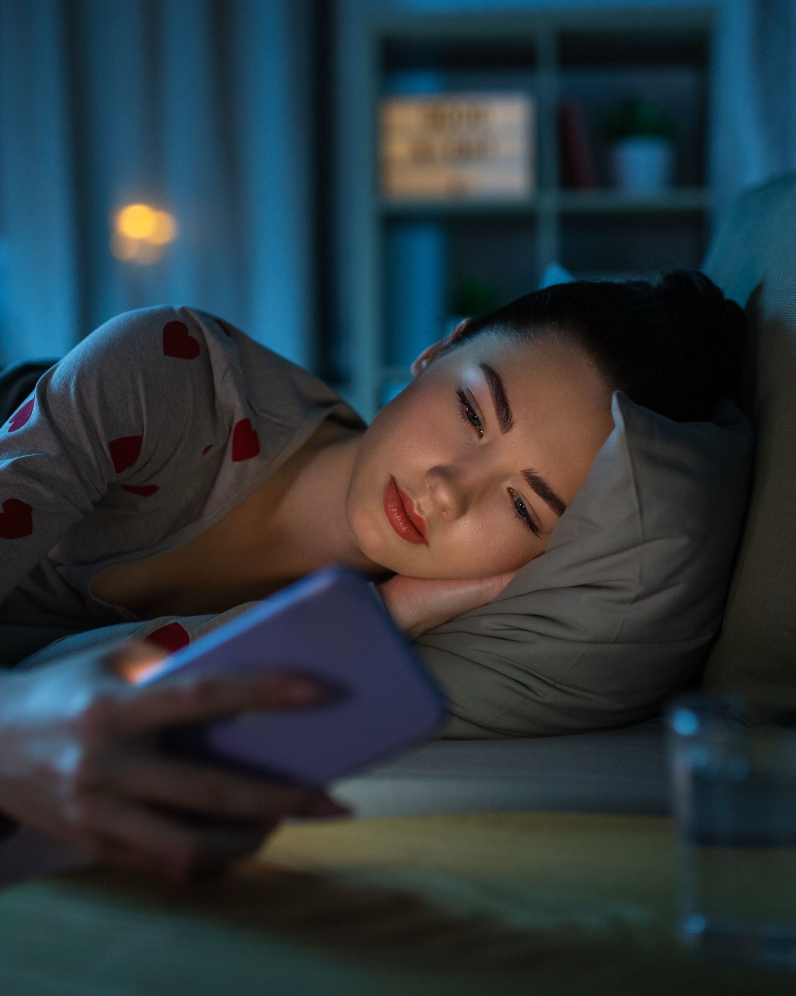 A woman lying in bed at night reading her phone, her face lit by the screen